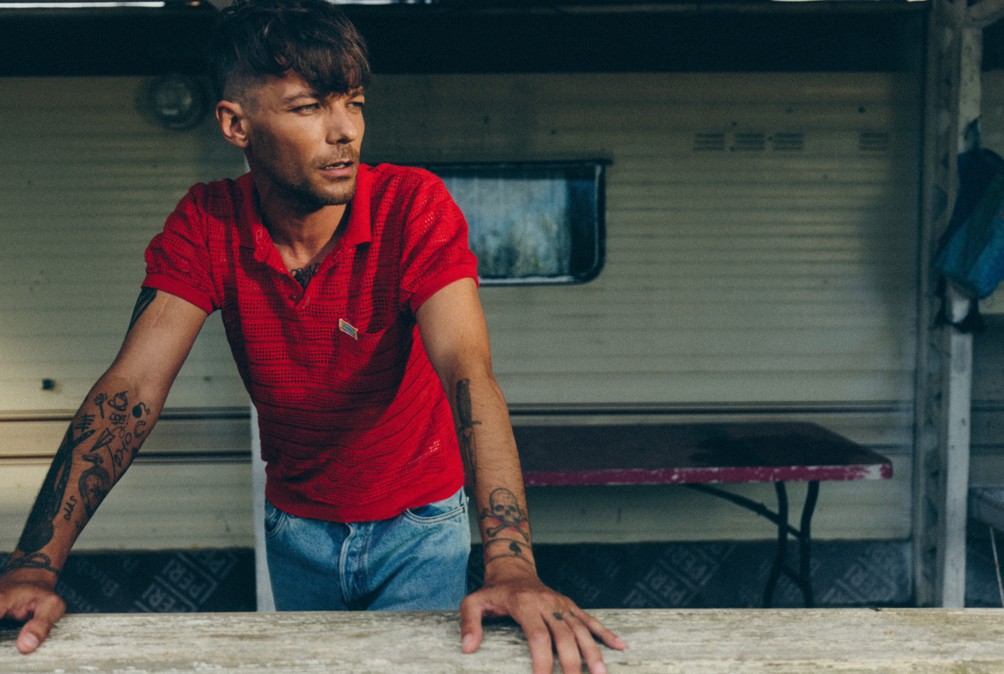 Musician Louis Tomlinson in a red top leaning on a wall